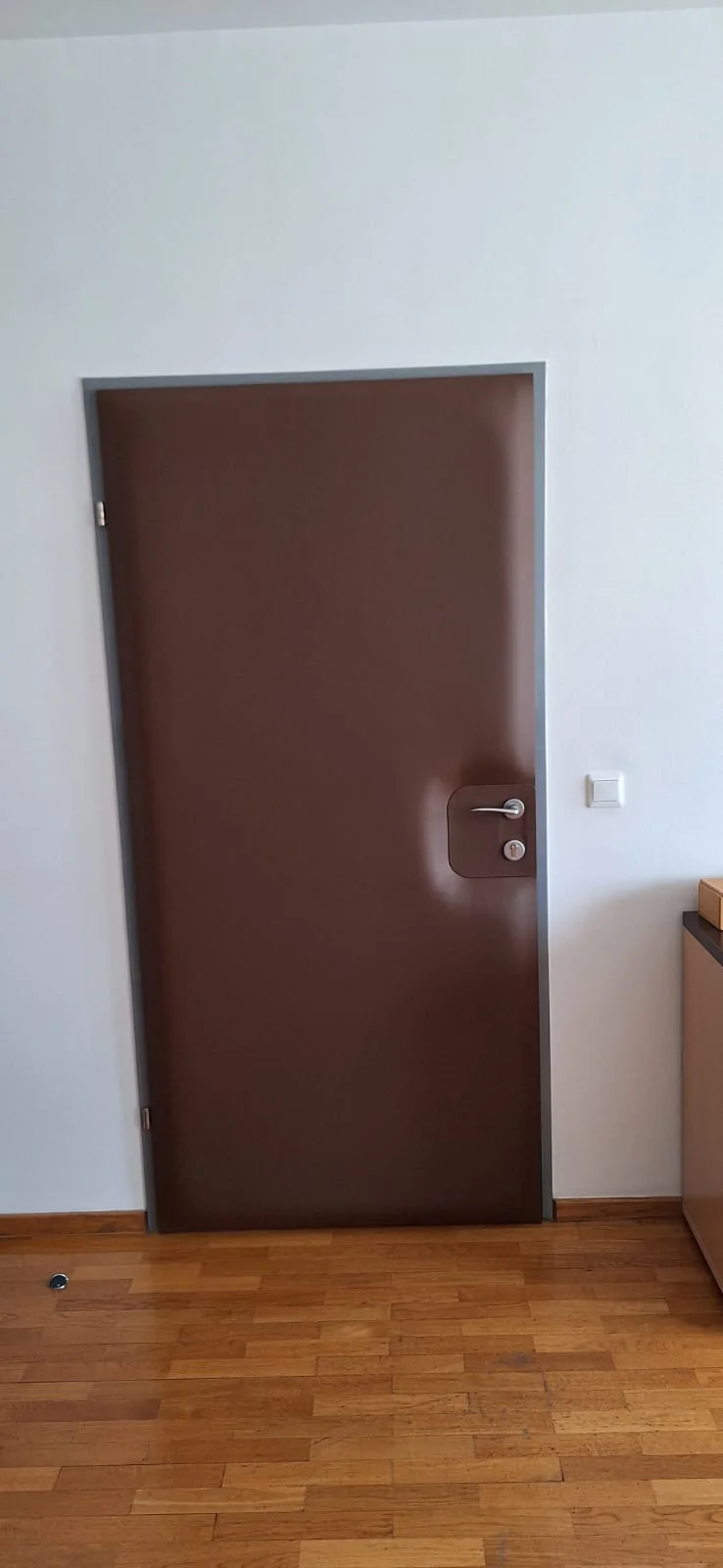 Smeđa tapecirana vrata s metalnom kvakom u svijetlom interijeru.