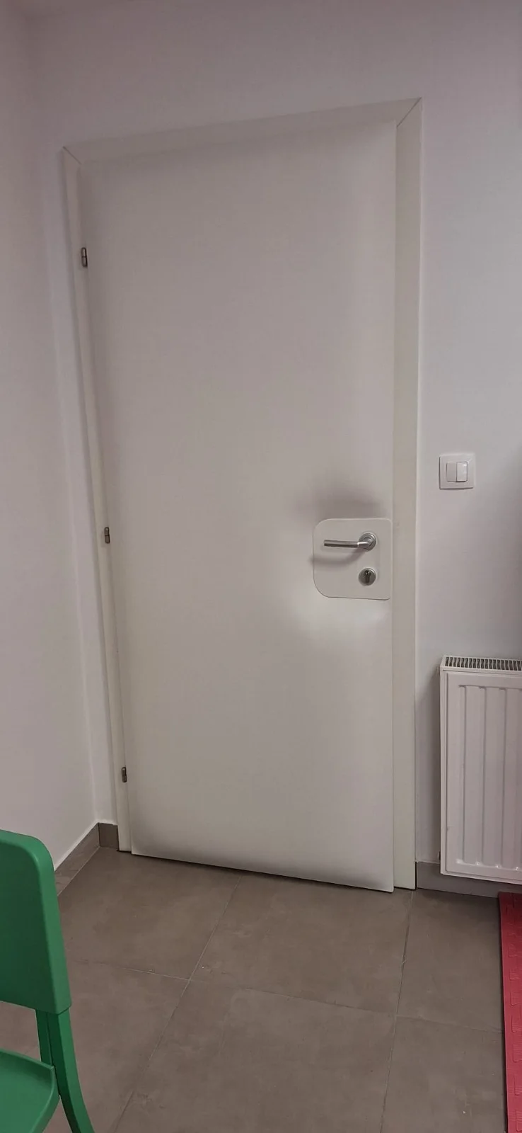 Bijela tapecirana vrata s metalnom kvakom uz radijator.